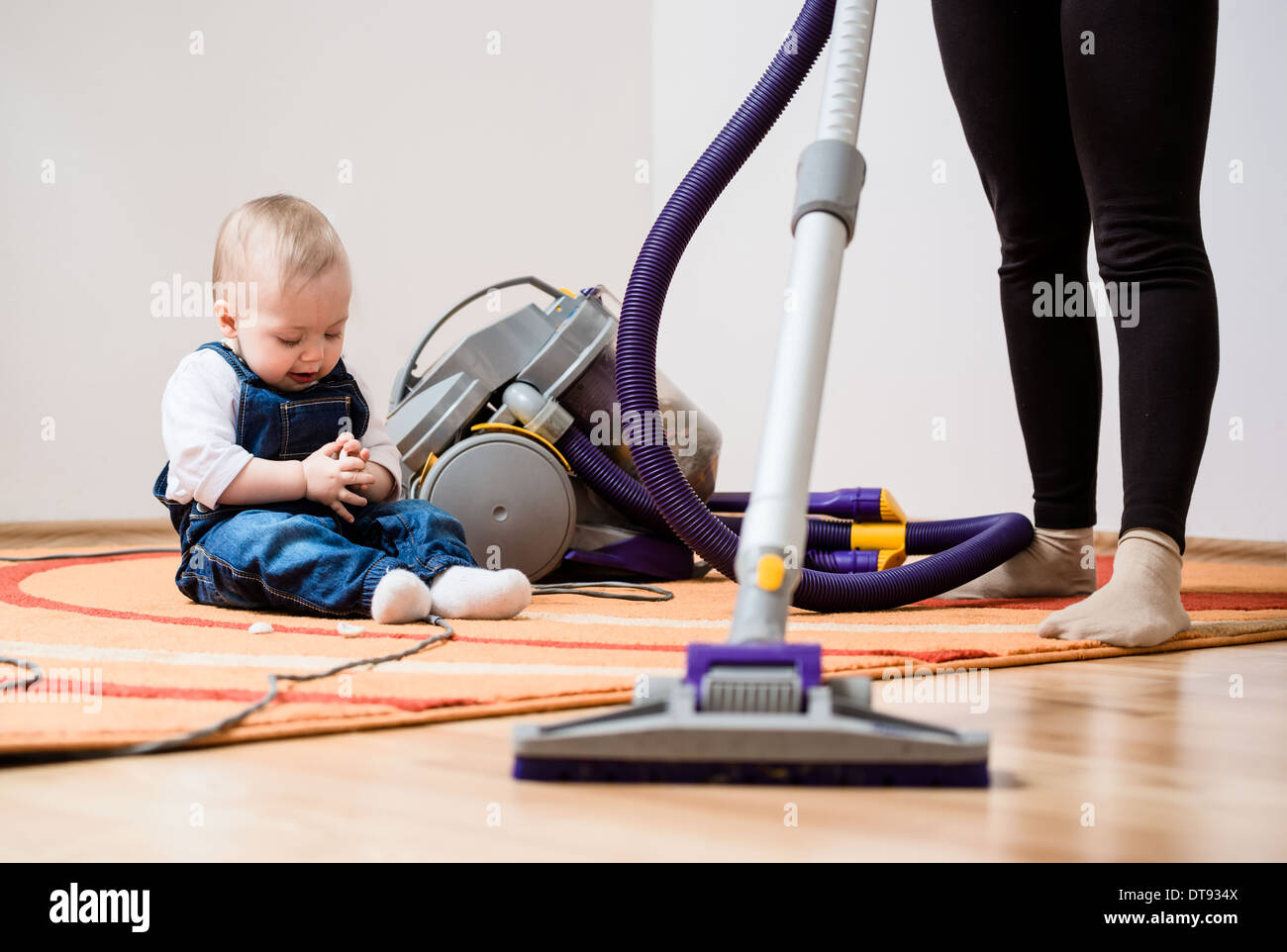 Le nettoyage de la chambre - woman with vacuum cleaner, baby sitting on floor Banque D'Images