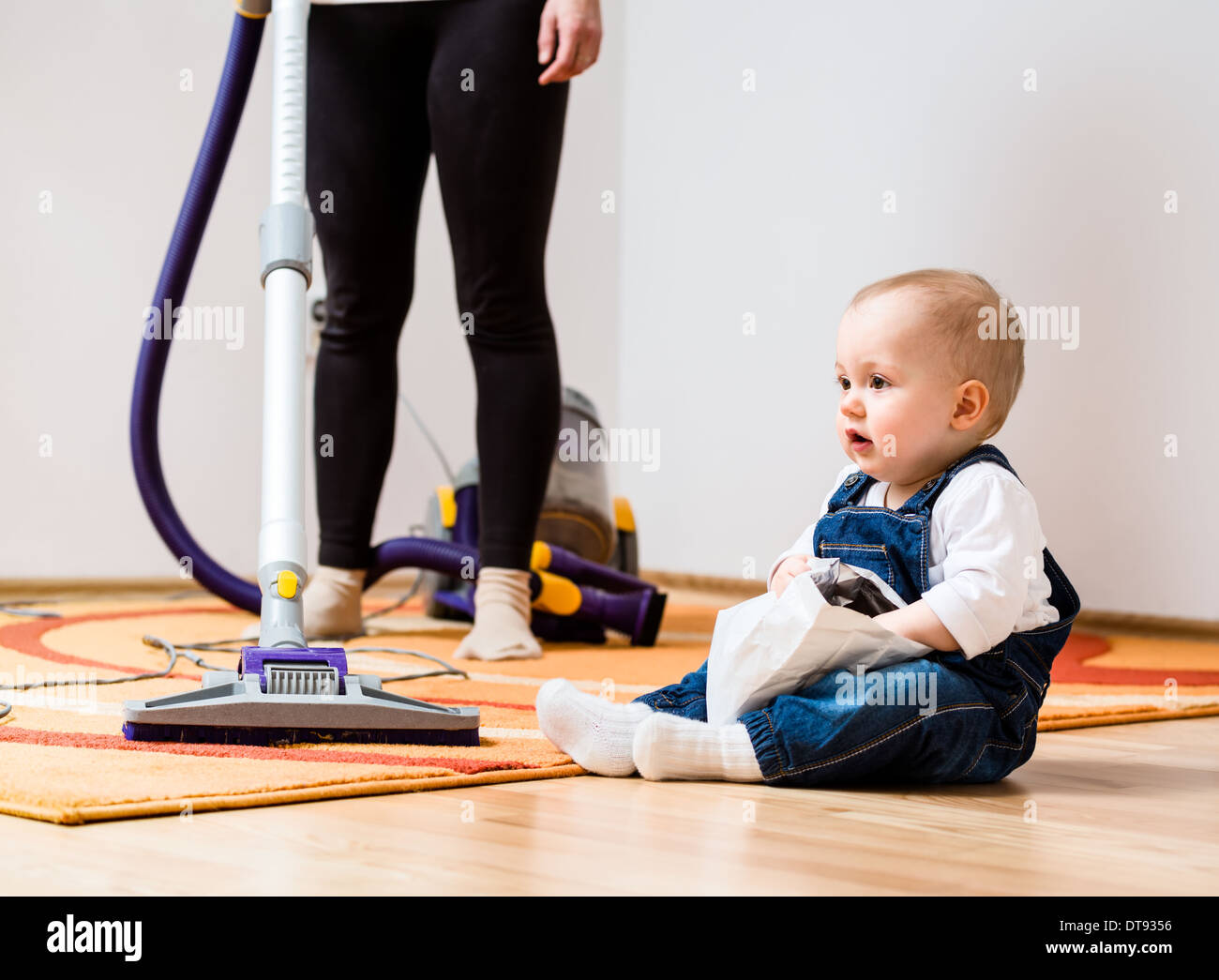 Le nettoyage de la chambre - woman with vacuum cleaner, baby sitting on floor Banque D'Images