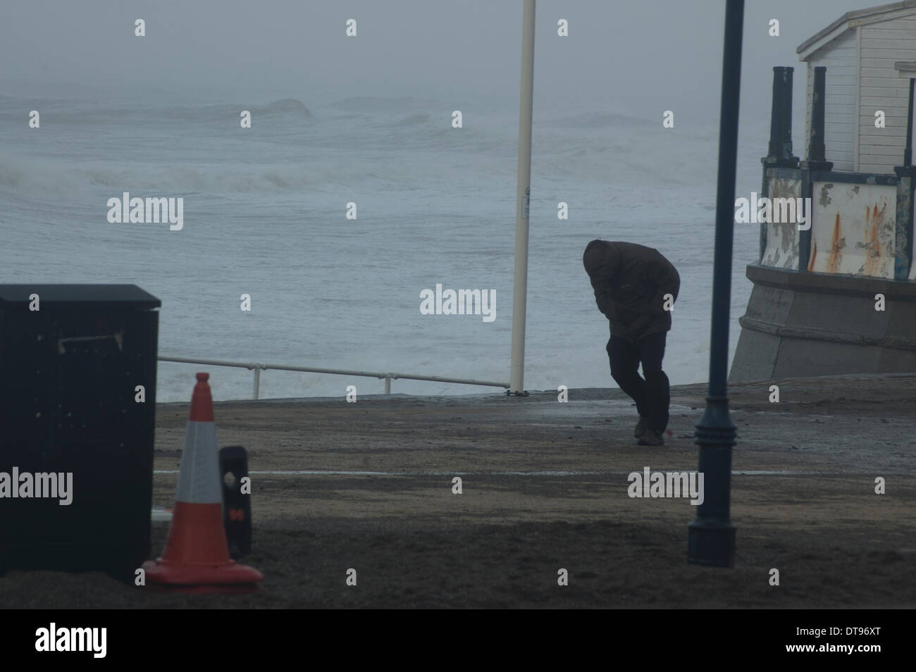 Aberystwyth, Pays de Galles, Royaume-Uni. 12 Février, 2014. L'homme peine à marcher contre le vent fort sur la promenade d'Aberystwyth. Le Met Office a publié sa première alerte rouge pour un risque potentiel pour la vie, avec Aberystwyth une fois de plus à la merci des conditions météorologiques extrêmes, cette fois avec des vents soufflant jusqu'à 100 mph battues de la promenade. Credit : Barry Watkins/Alamy Live News Banque D'Images