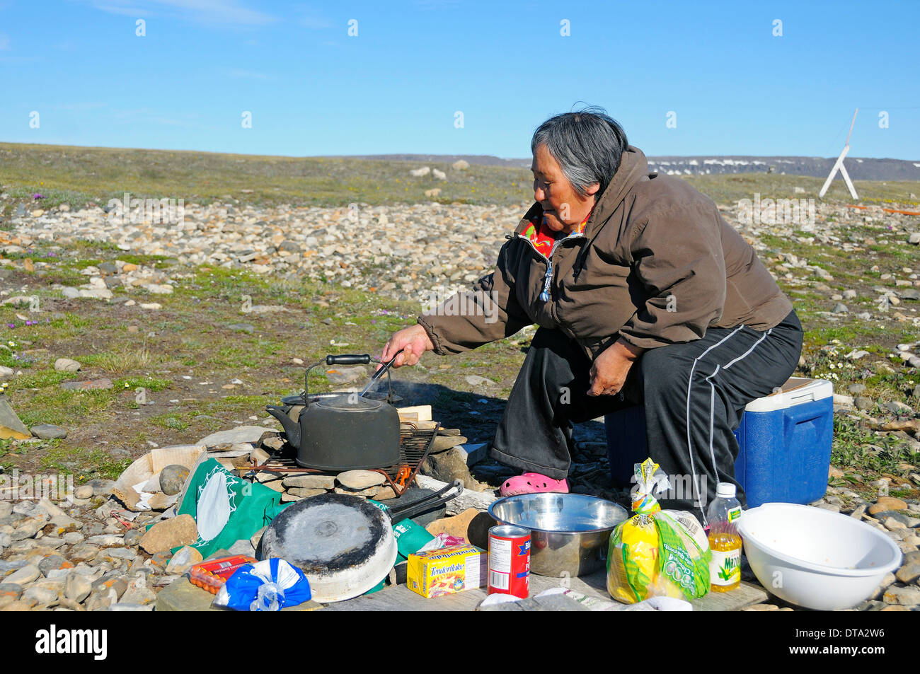 Femme du peuple Inuit cuisson sur un feu de camp dans la toundra, l'île Victoria, anciennement l'île Holman, village d'Ulukhaktok Banque D'Images