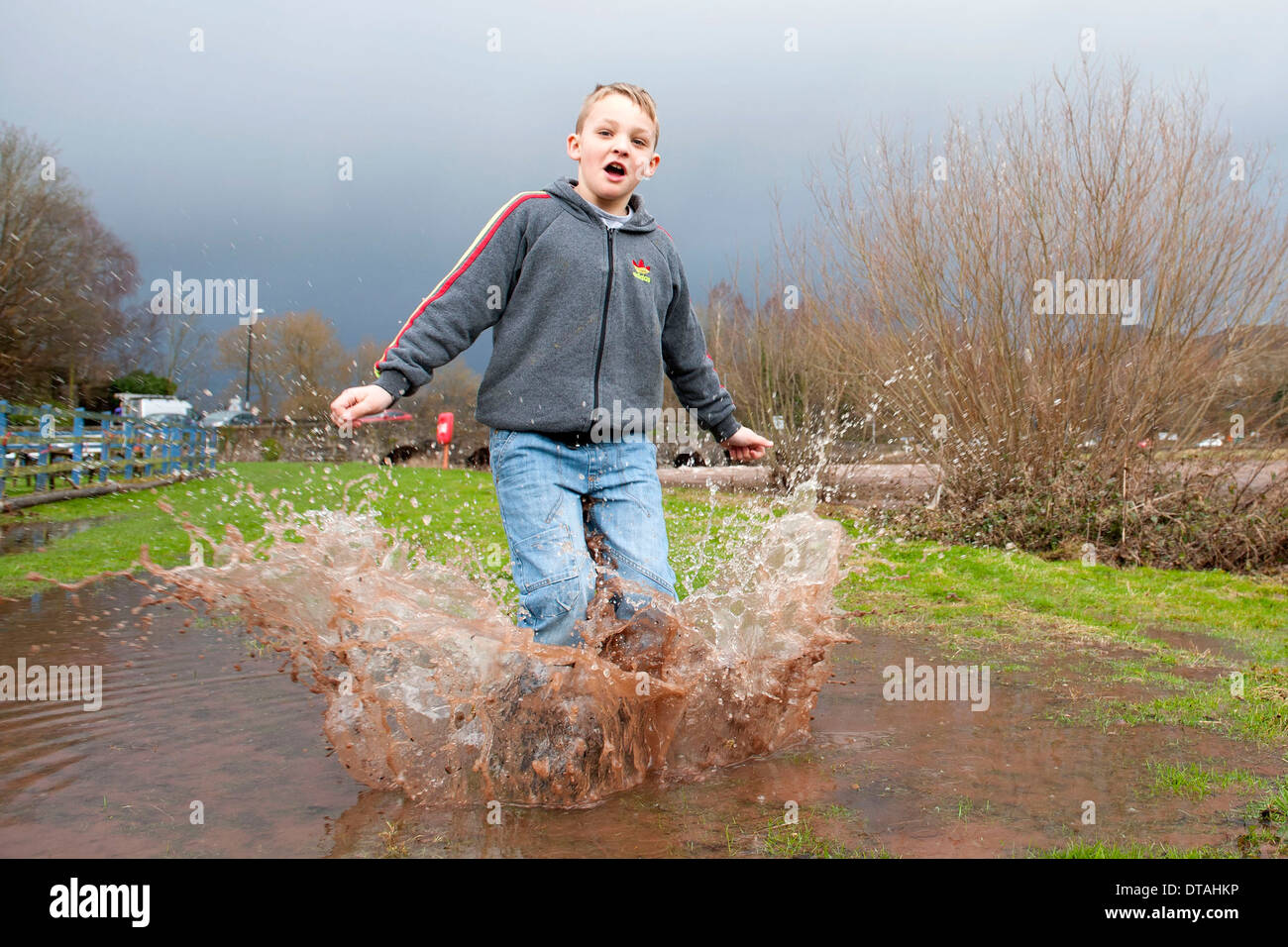 Un jeune garçon profitant du temps pluvieux de sauter dans une flaque d'eau et les projections d'eau. Banque D'Images