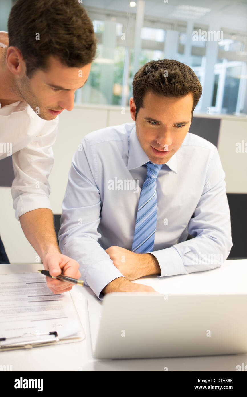 Deux beaux hommes travaillant ensemble sur un ordinateur portable au bureau Banque D'Images