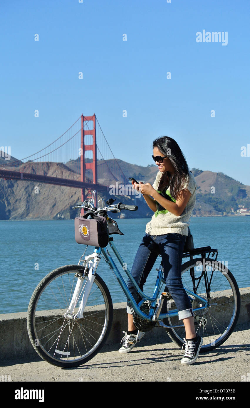 Jolie fille asiatique textes sur location vélo sur Presidio Pier Banque D'Images