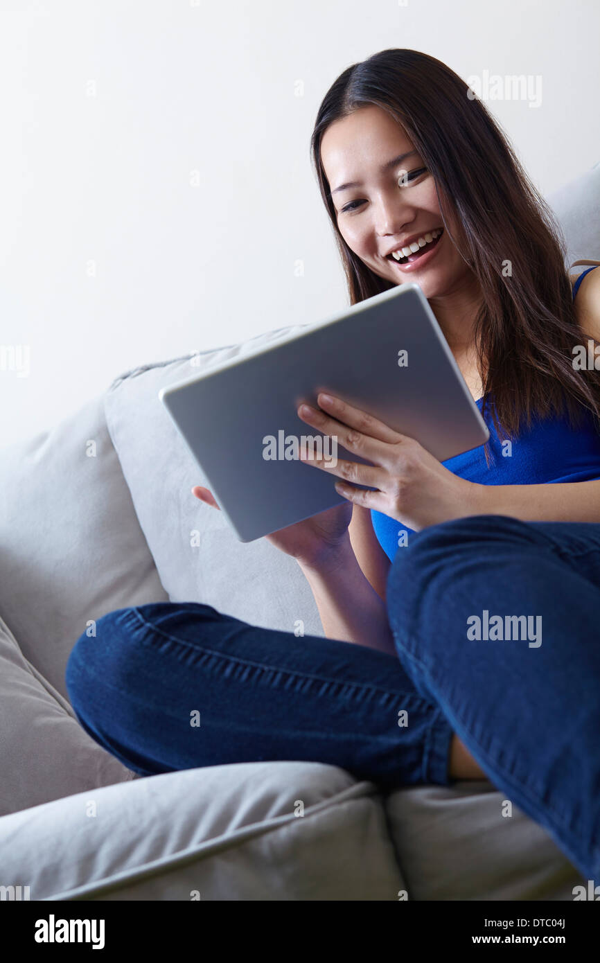 Young woman sitting on sofa using digital tablet Banque D'Images