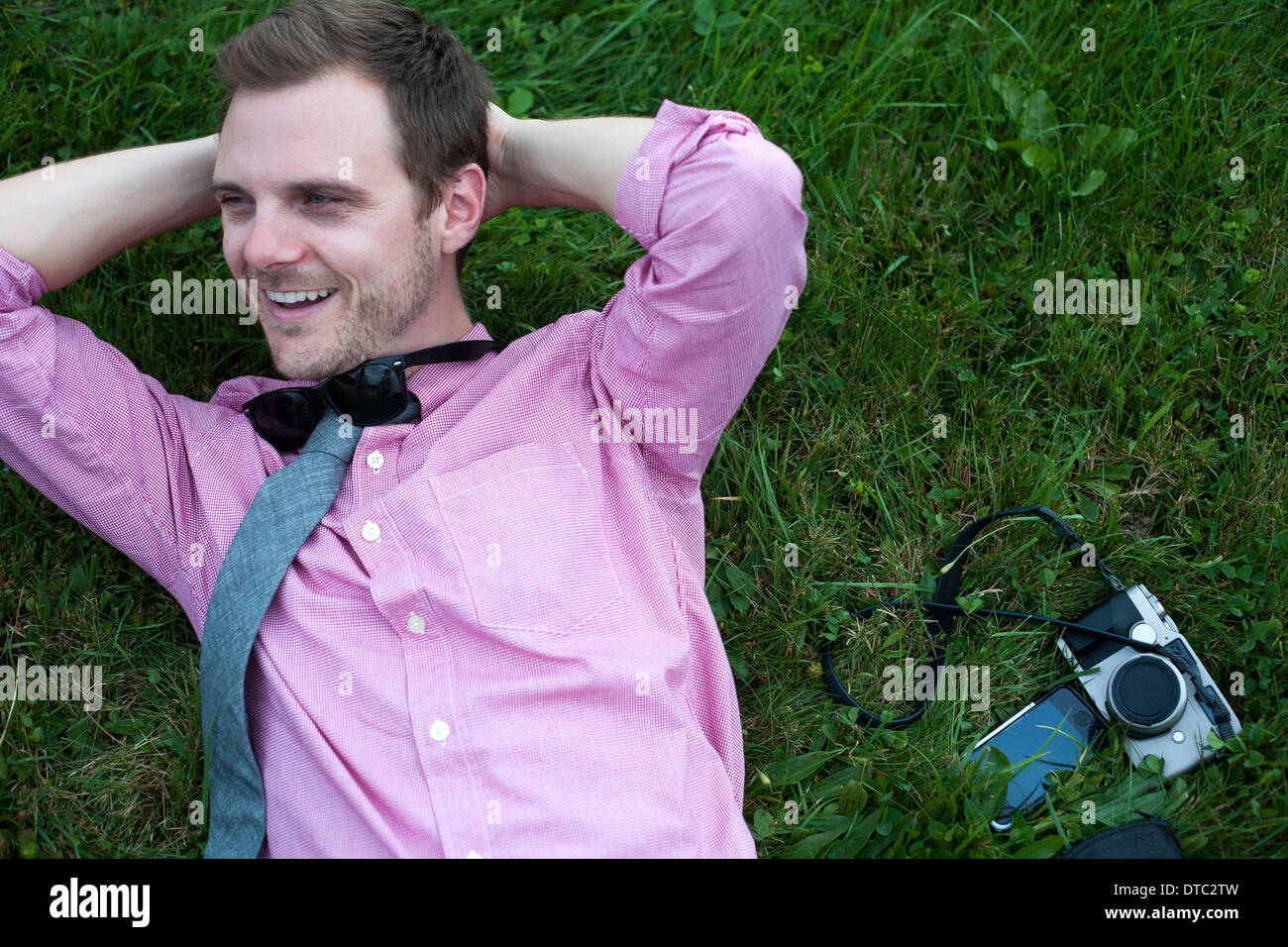 Mid adult man avec caméra et smartphone relaxing on grass Banque D'Images