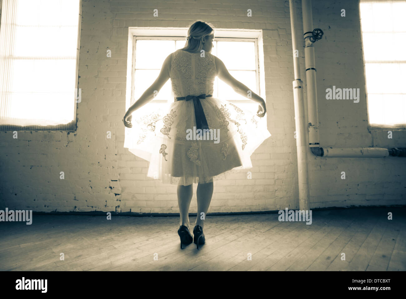 Un 16-year-old woman wearing a white lace vintage robe, se tient devant une fenêtre dans l'usine corset Cortland. Banque D'Images