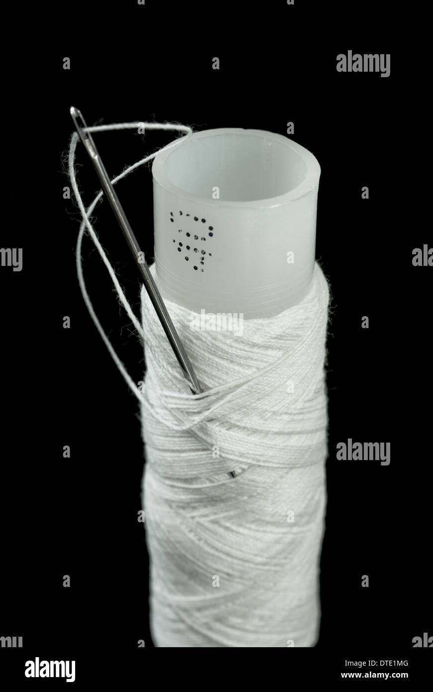 Bobine de fil blanc avec une aiguille sur un fond noir Banque D'Images