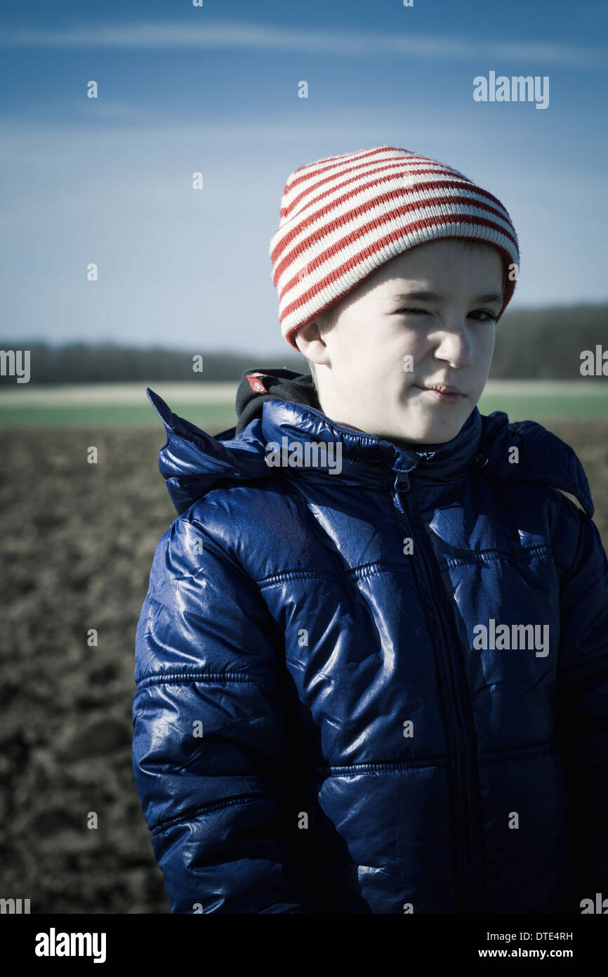 Jeune garçon debout sur les terres agricoles avec un clin. Banque D'Images