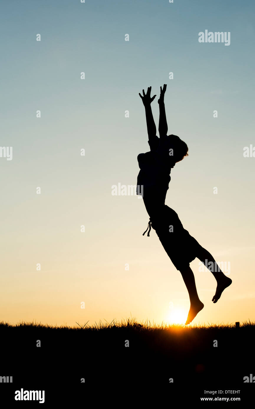 Garçon sautant avec ses mains en l'air au coucher du soleil. Silhouette Banque D'Images