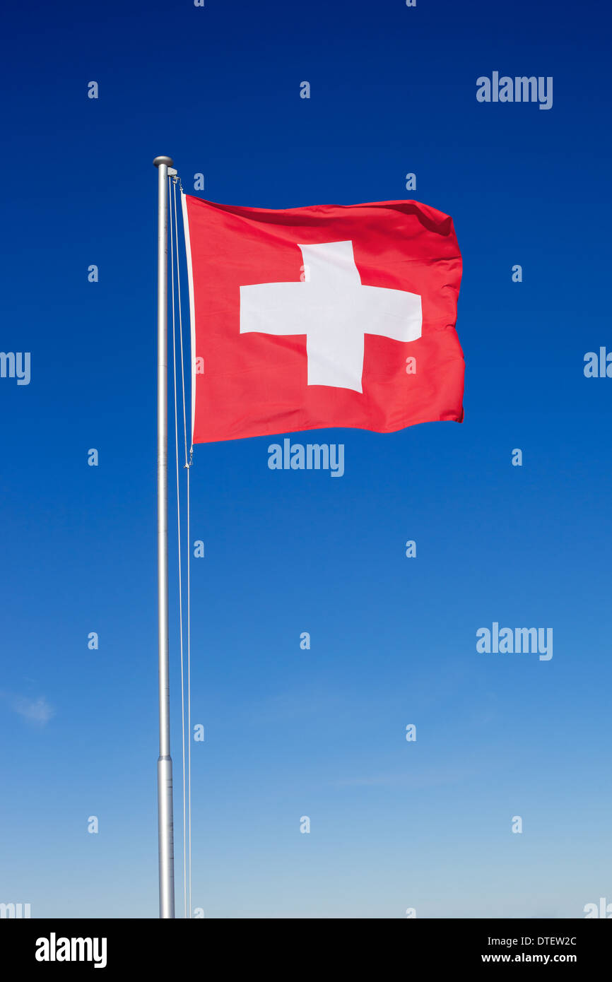 Le drapeau national de la Suisse battant sur un poteau de métal contre un ciel bleu clair. Banque D'Images