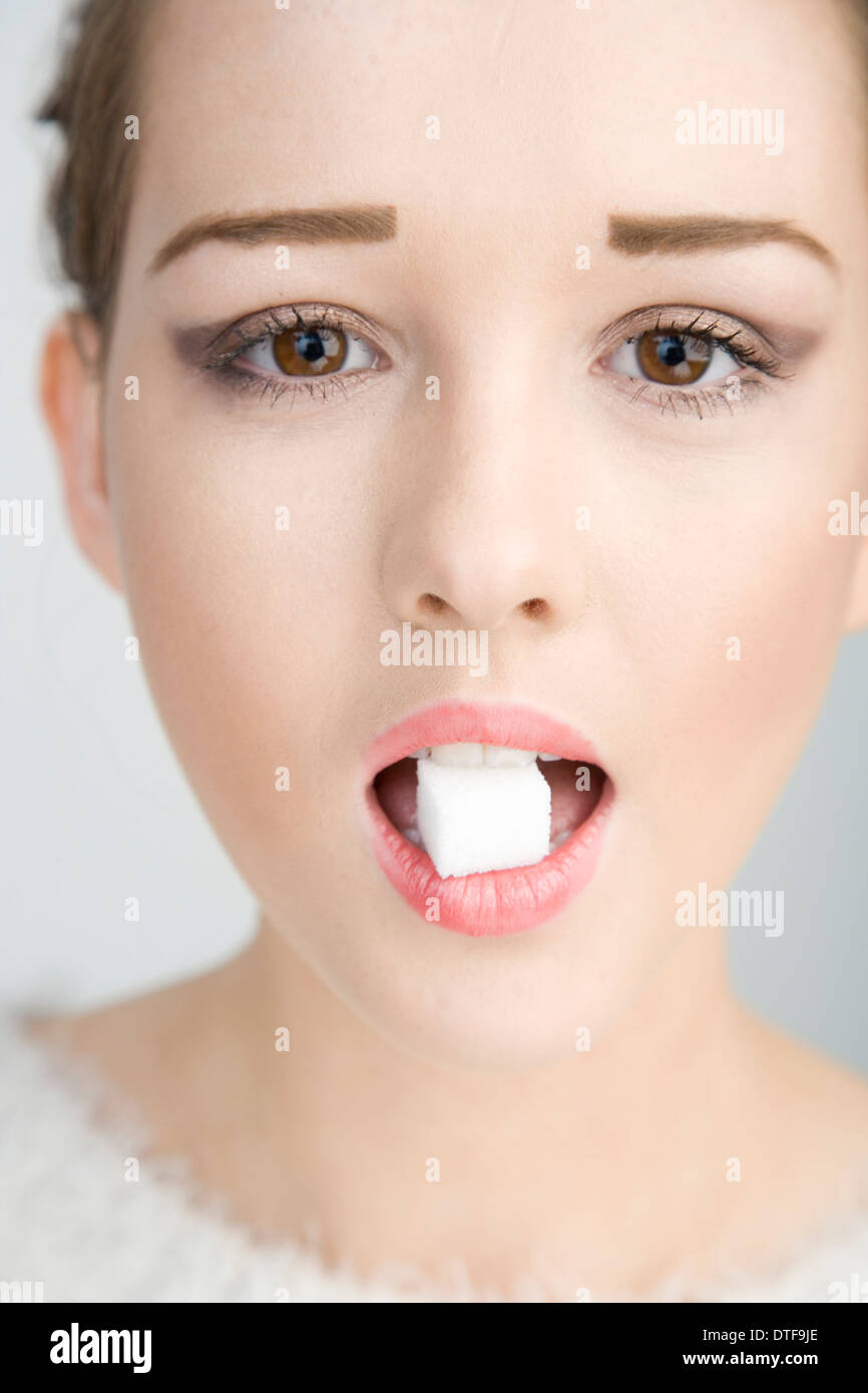 Un joli teenage girl holding un cube de sucre dans sa bouche. Banque D'Images
