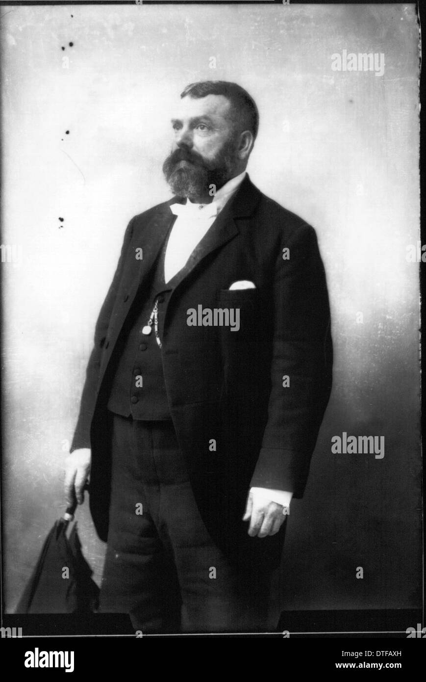 Cette photographie de portrait vintage capture un homme barbu dans un costume, tenant un parapluie. L'image reflète la mode et le style d'une période historique particulière, donnant un aperçu de l'apparence personnelle et du caractère du sujet. Banque D'Images