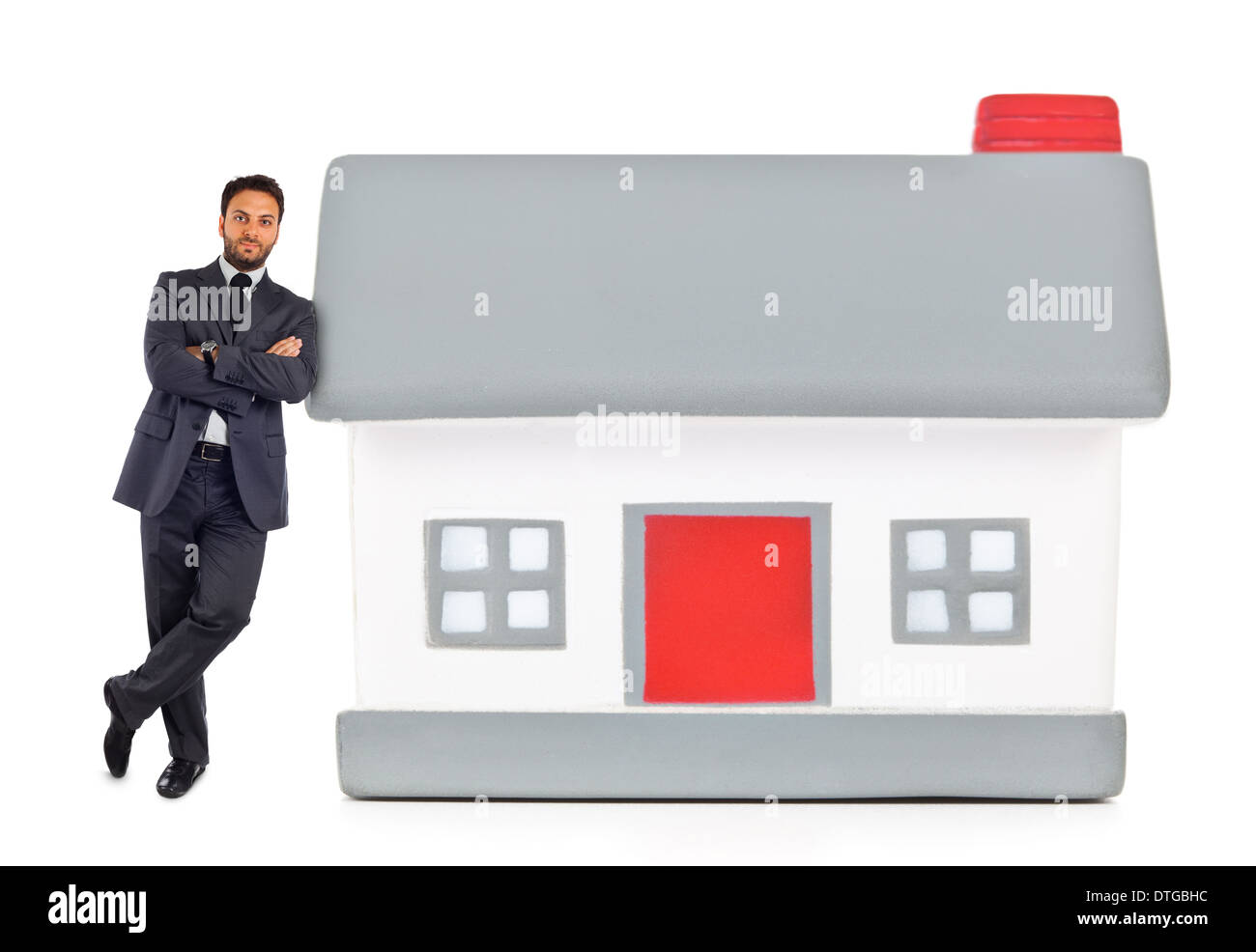 Businessman leaning against a miniature house on white. Banque D'Images