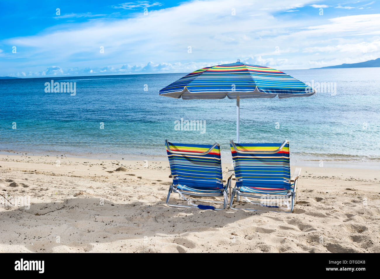 Deux chaises de plage avec parasol sur le bord de l'eau d'une plage tropicale Banque D'Images