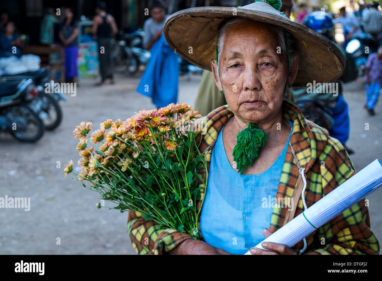 Vieille Femme birmane de marcher dans les rues de marché Nyaung U près de Bagan au Myanmar avec quelques fleurs. Banque D'Images