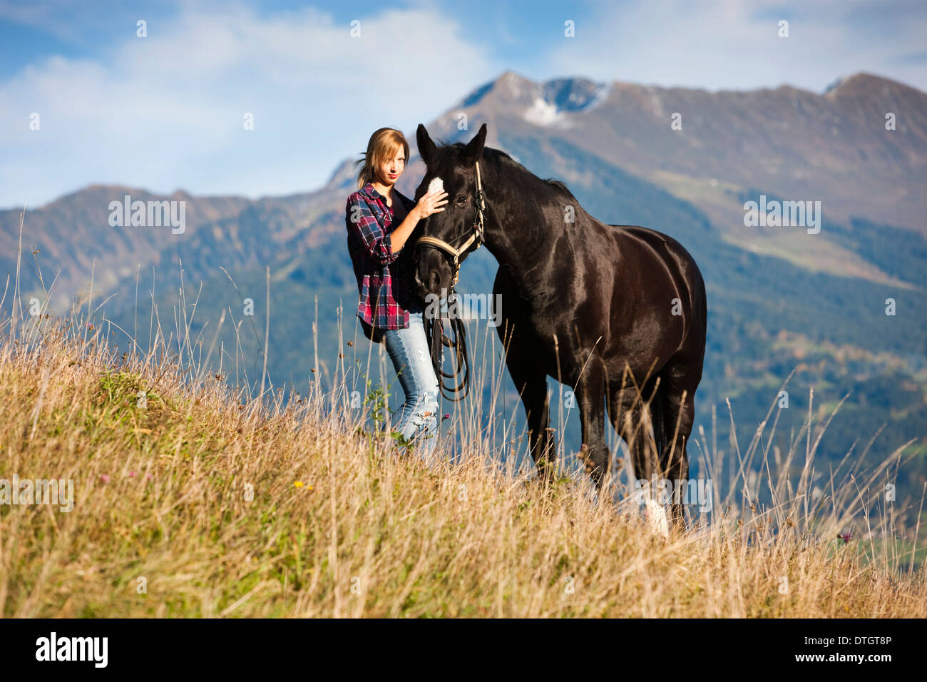 Une jeune femme et un cheval hanovrien noir debout sur une prairie de montagne en automne, Tyrol du Nord, Autriche Banque D'Images
