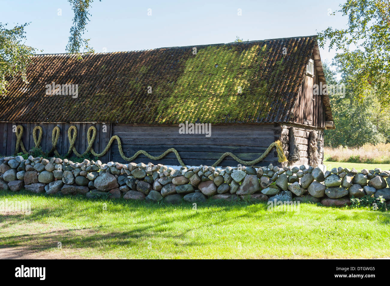 Vieille maison en bois avec un toit recouvert de mousse et d'équilibriste sur mur. Clôture en pierre de galets en face de la maison. Banque D'Images