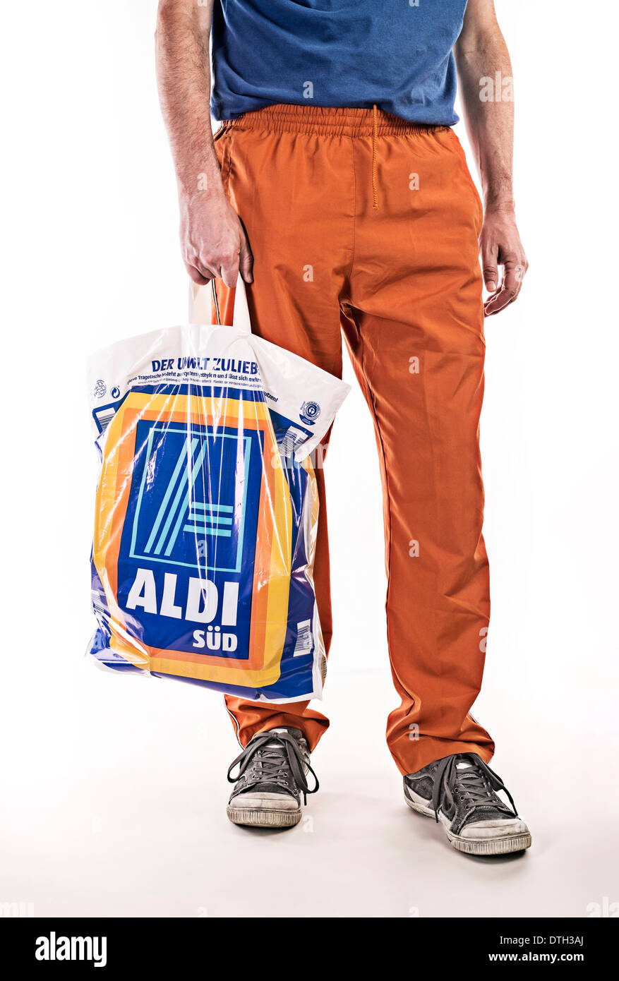 La partie inférieure du corps d'un homme avec survêtement, transportant un sac en plastique alimentaire de discounter Aldi. Banque D'Images