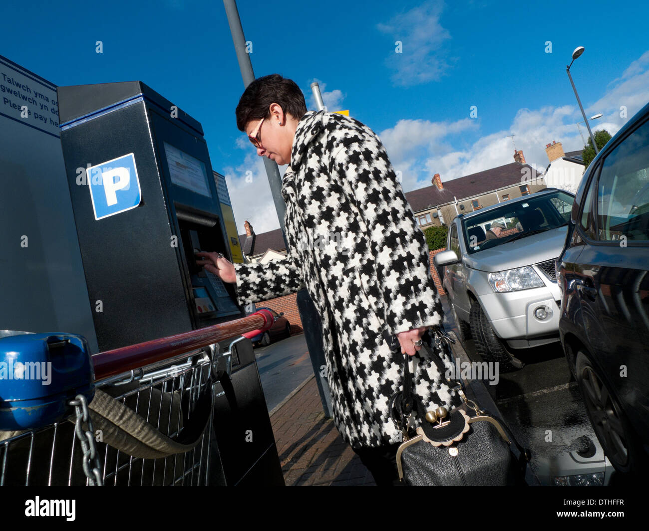 Une femme dans un tissu imprimé houndstooth manteau contrôle mettant l'argent dans une machine dans un parking parking supermarché UK KATHY DEWITT Banque D'Images