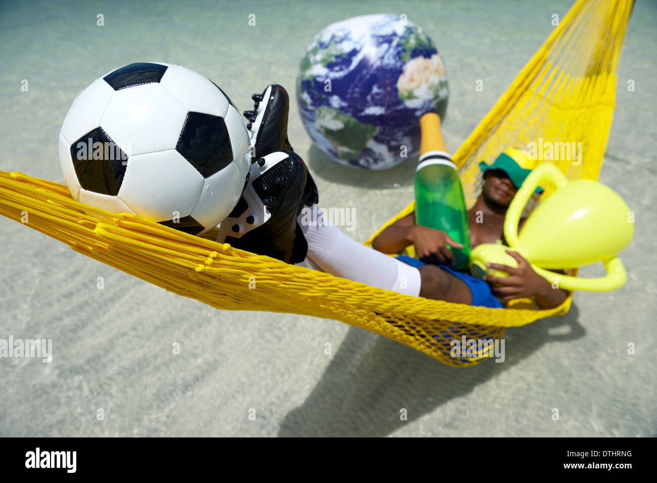 Le joueur de soccer brésilien Champion célébrer en vous relaxant dans son hamac avec football, bouteille de champagne, et le trophée que le monde Banque D'Images