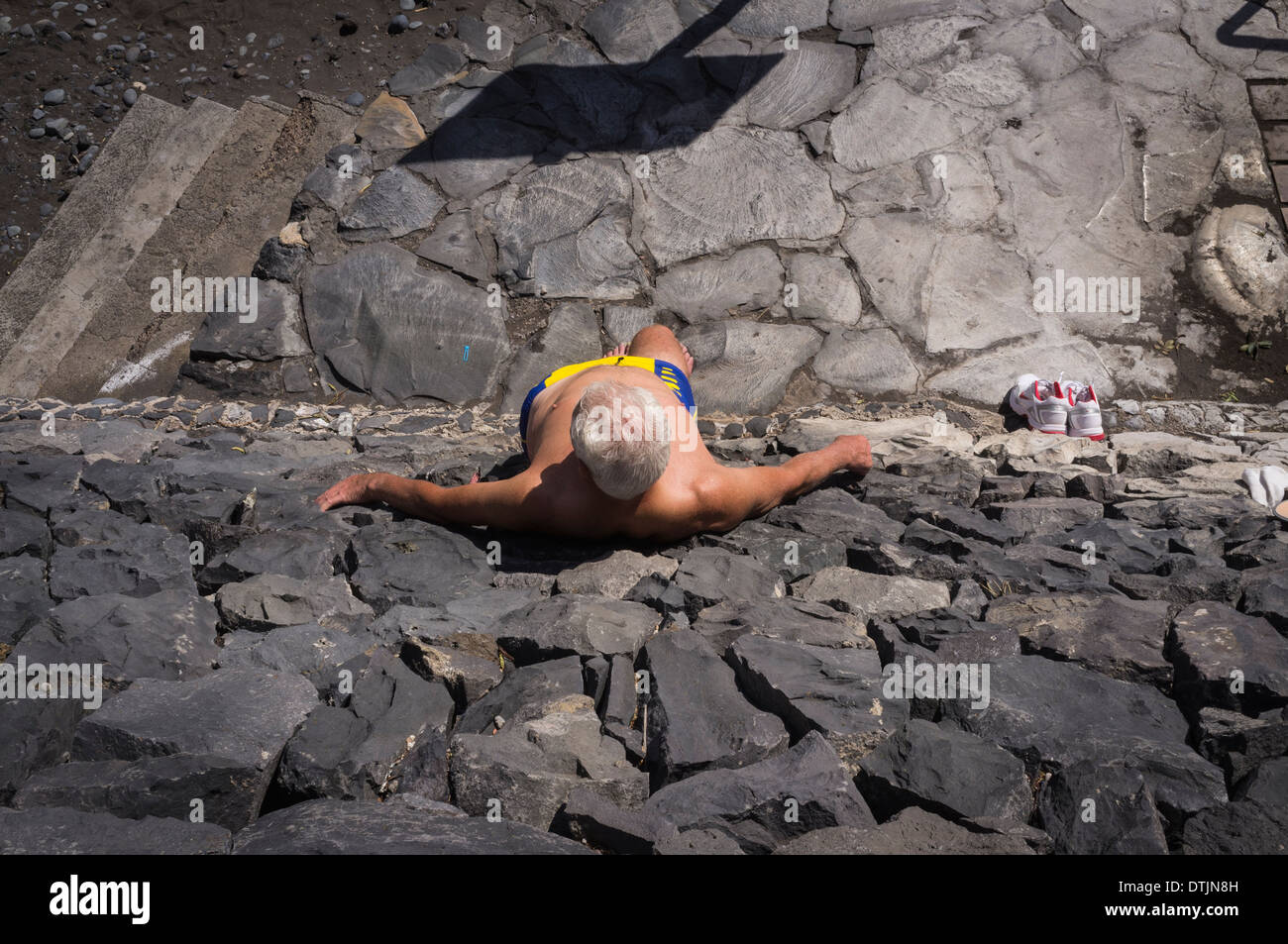 L'homme soleil debout contre un mur en pierre volcanique à Playa San Juan beach, Tenerife, Canaries, Espagne Banque D'Images