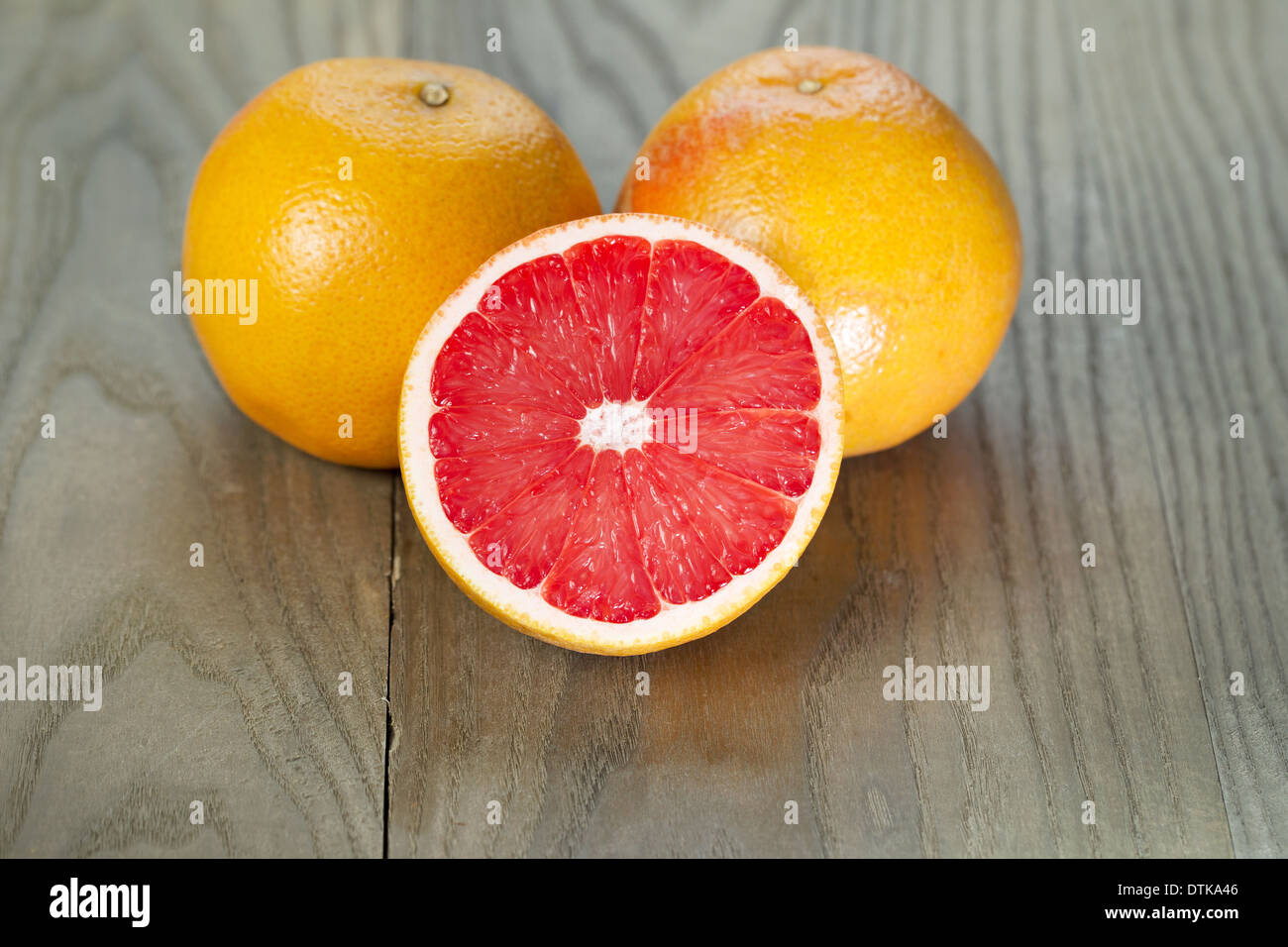 Photo horizontale de tranches de Pamplemousse ruby red la moitié en face de deux fruits sur bois vieilli Banque D'Images