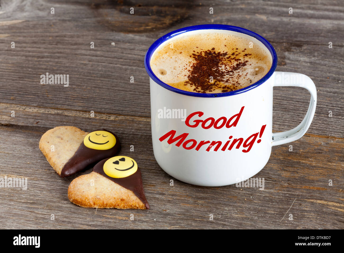 Tasses en émail avec du café chaud et deux biscuits en forme de coeur sur une planche en bois rustique avec le mot 'Bonjour' sur la tasse Banque D'Images