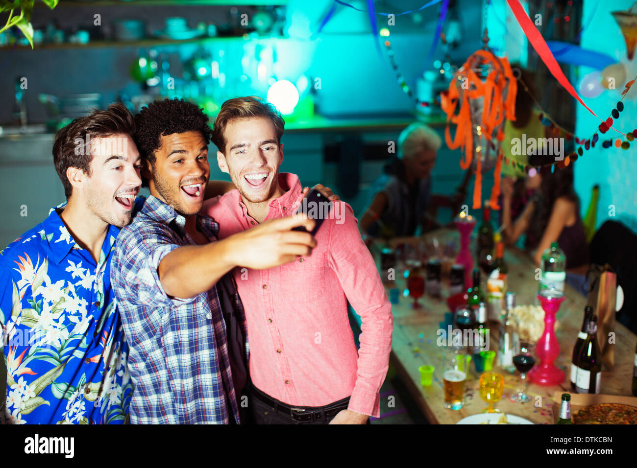 Les hommes prendre des auto-portraits avec camera phone at party Banque D'Images