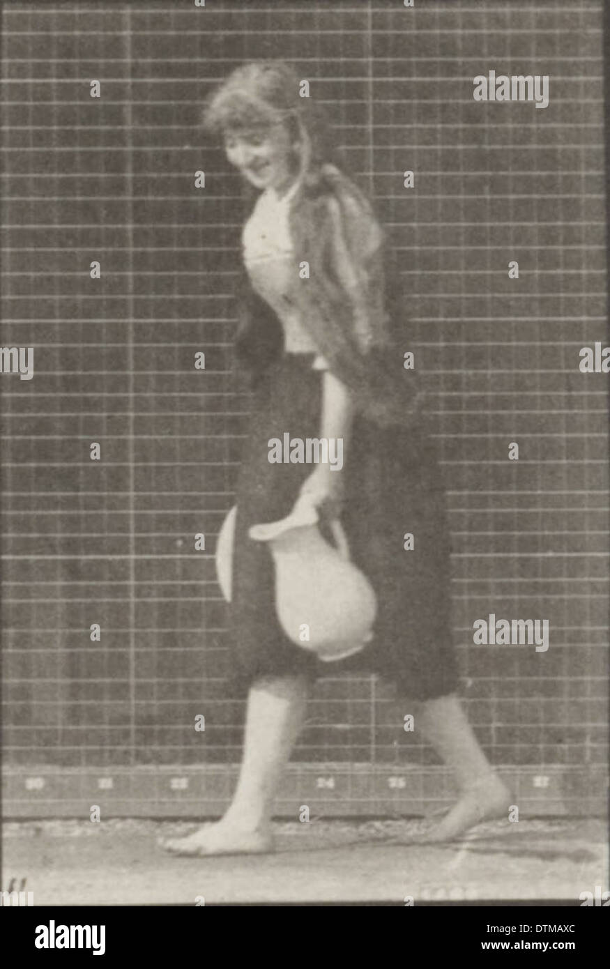 Photographie d'une femme en robe longue soulevant et vidant un bassin d'eau tout en tournant, capturant son mouvement. Banque D'Images