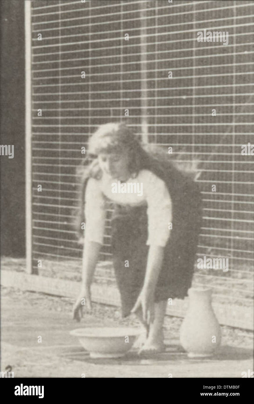 Une femme dans une robe longue est montrée soulevant et vidant un bassin d'eau tout en tournant dans cette photographie vintage. Banque D'Images