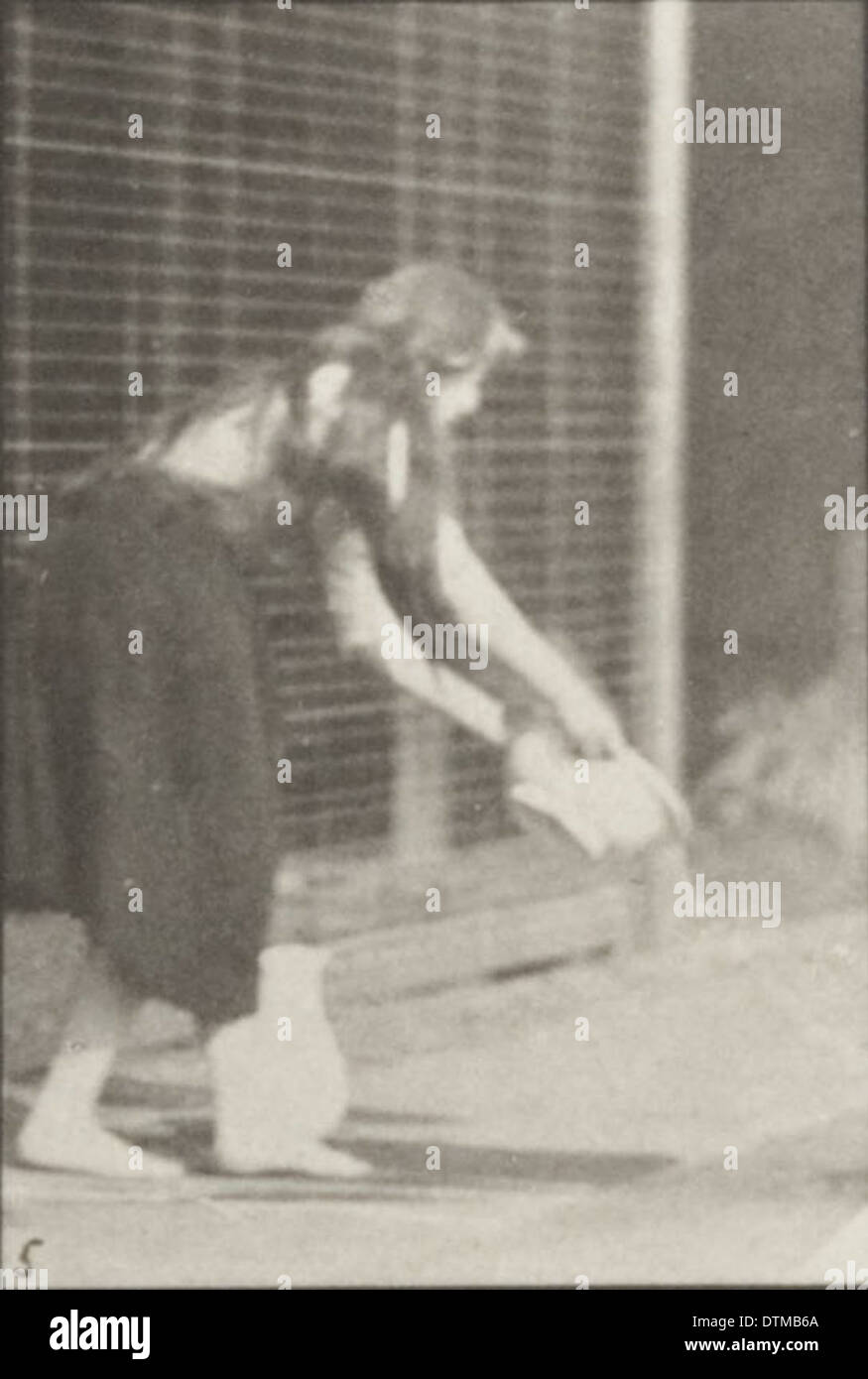 Une femme dans une robe longue soulève et vide un bassin d'eau tout en tournant. La photographie capture le mouvement et la grâce de la scène. Banque D'Images