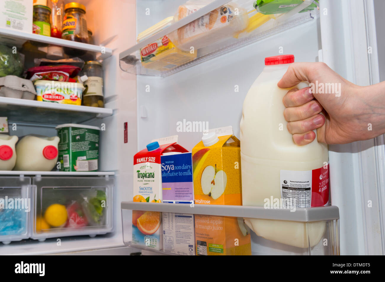 Une main tirant sur une bouteille de lait à partir d'une porte de réfrigérateur bien approvisionné Banque D'Images