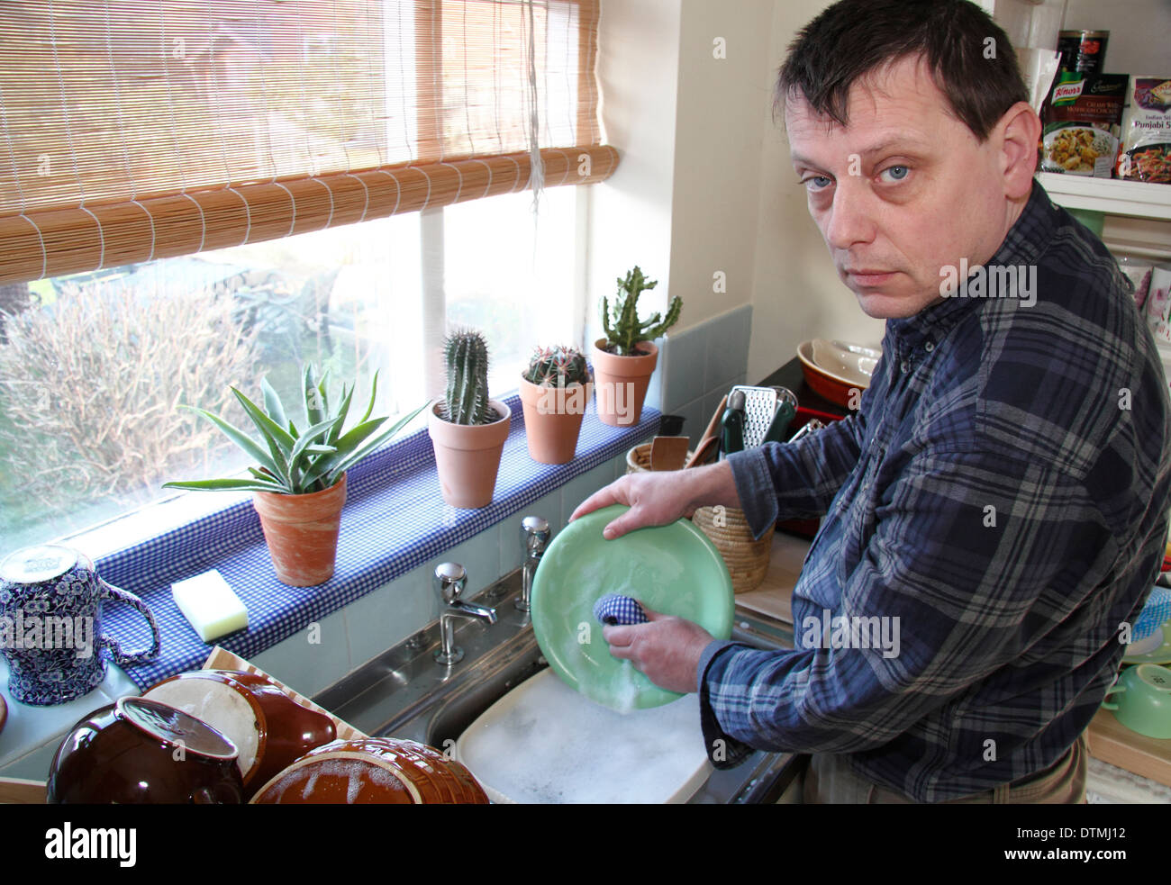 Man washing up pots avec peu d'enthousiasme à un évier de cuisine à la maison, England, UK Banque D'Images