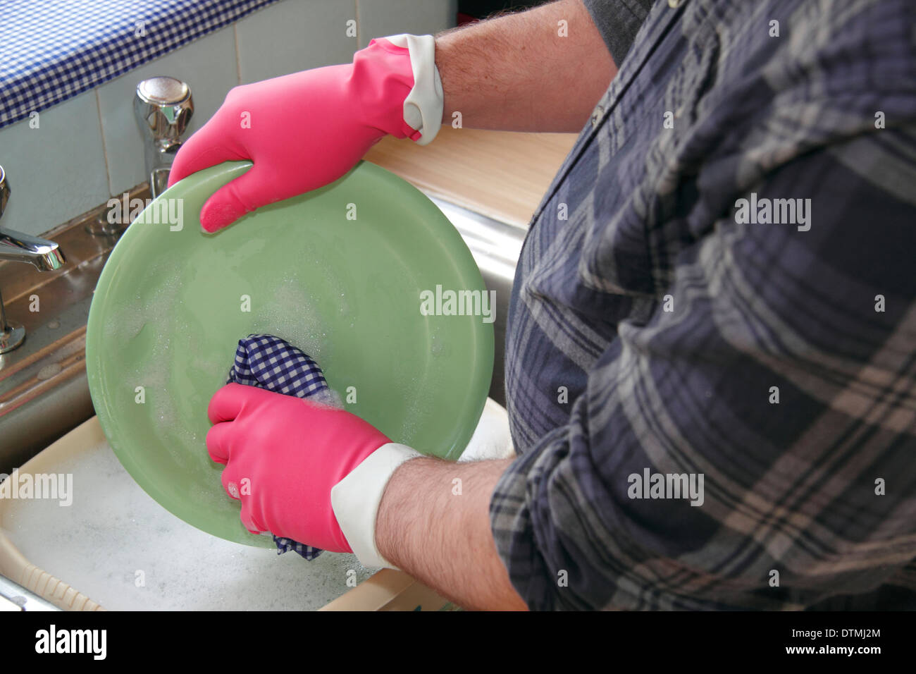 Man les pots portant des gants en caoutchouc rose à un évier de cuisine à la maison, England, UK Banque D'Images