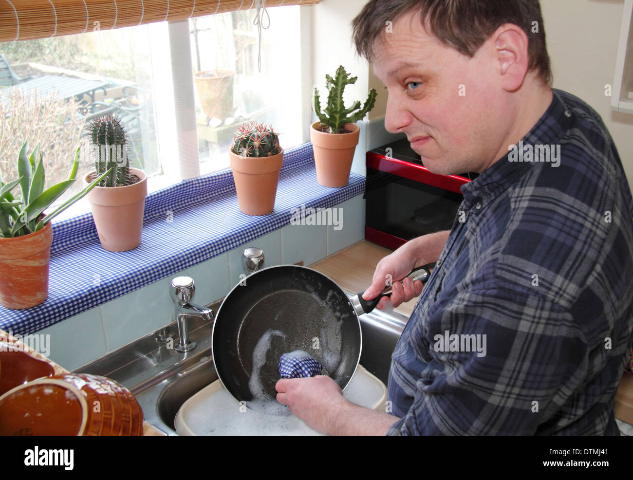 Man washing up pots/poêle avec peu d'enthousiasme à un évier de cuisine à la maison, England, UK Banque D'Images