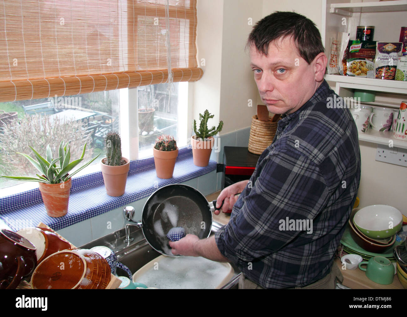 Man washing up pots avec peu d'enthousiasme à un évier de cuisine à la maison, England, UK Banque D'Images