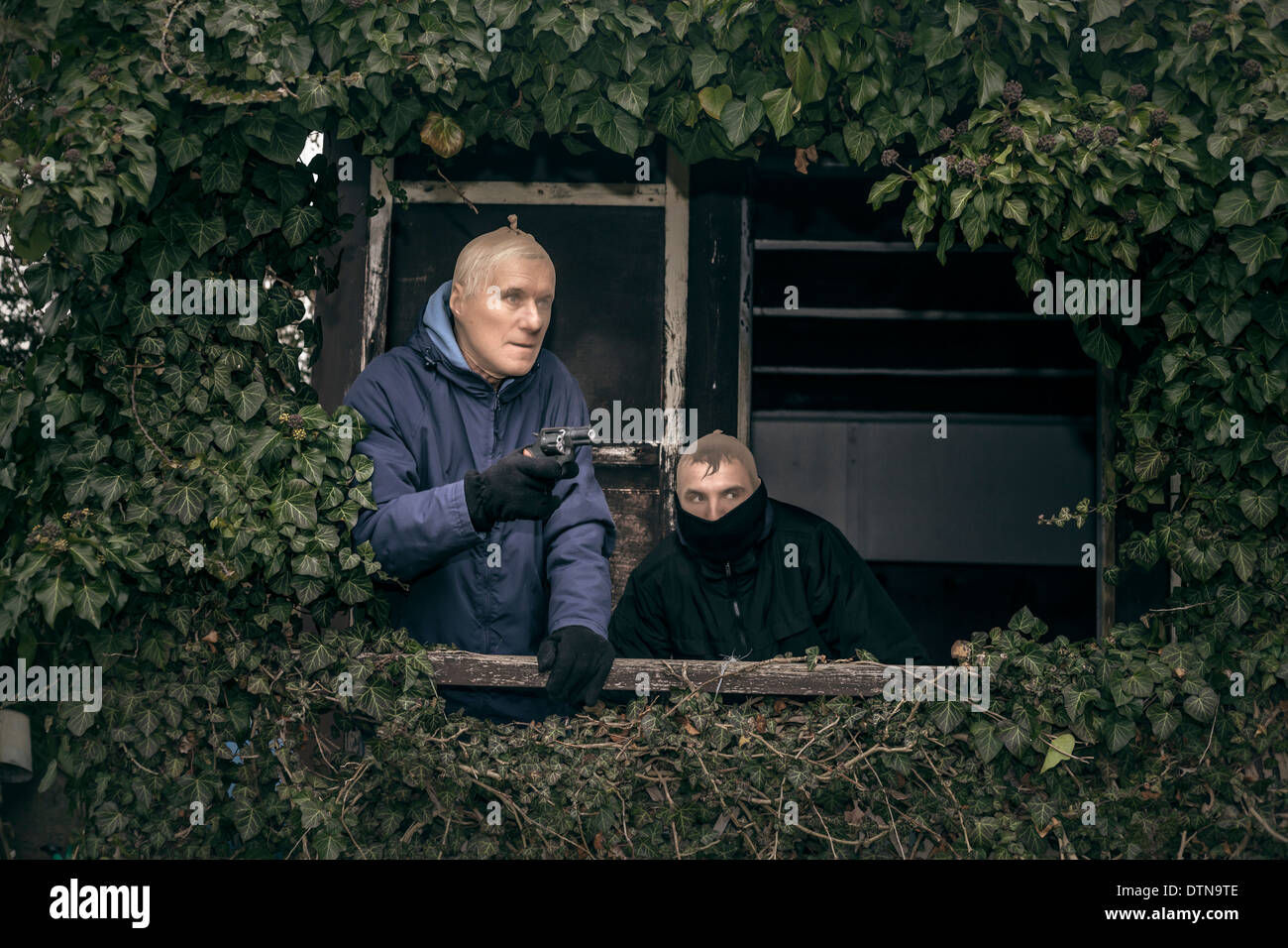 Deux hommes armés masqués se cachent sur de vieux porche envahi par la cabine. Banque D'Images