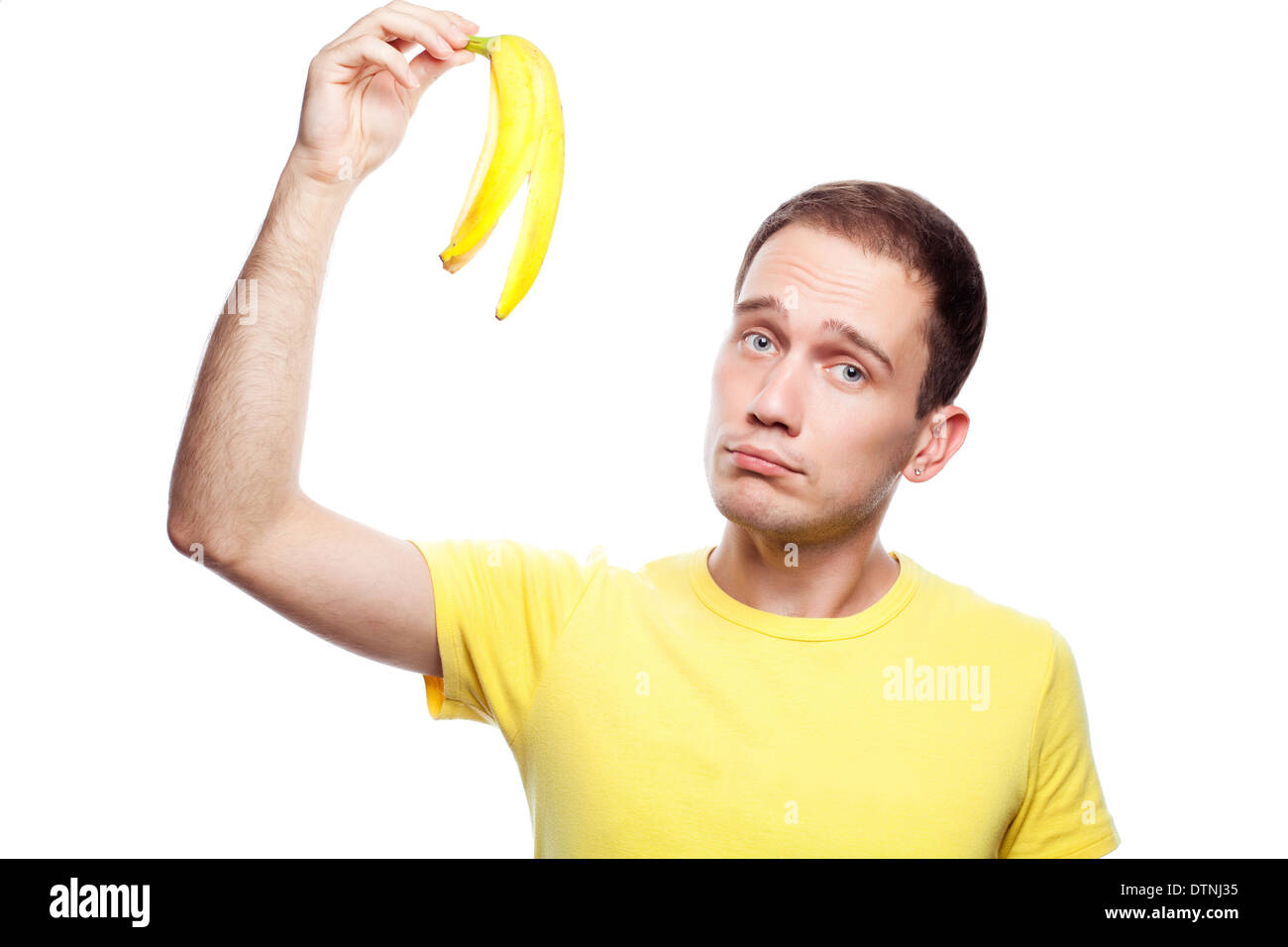 Déçu beau gars en jaune t-shirt holding peau de banane sur fond blanc Banque D'Images