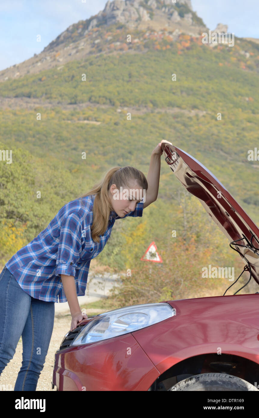 Jeune femme près de voiture cassée a besoin d'aide à la recherche sous le capot ouvert Banque D'Images