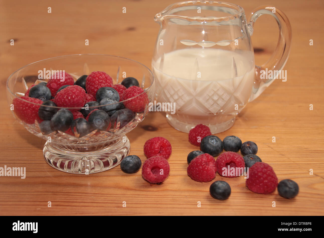 Les framboises et les bleuets dans un cristal de verre sundae et la crème dans un pot sur une table en pin (3 de 11) Banque D'Images