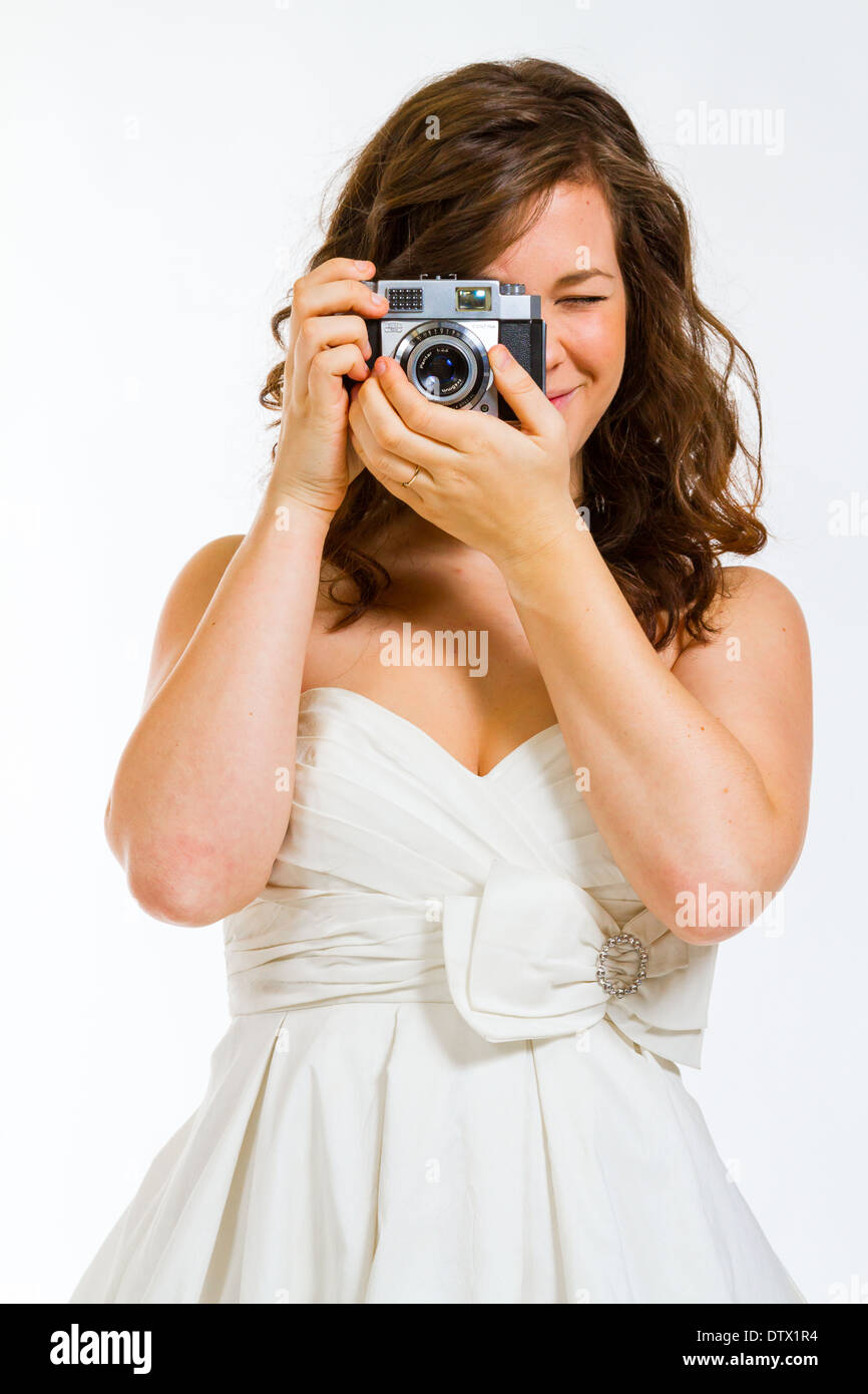 Une belle épouse tenant un appareil photo en studio contre un fond blanc. Banque D'Images