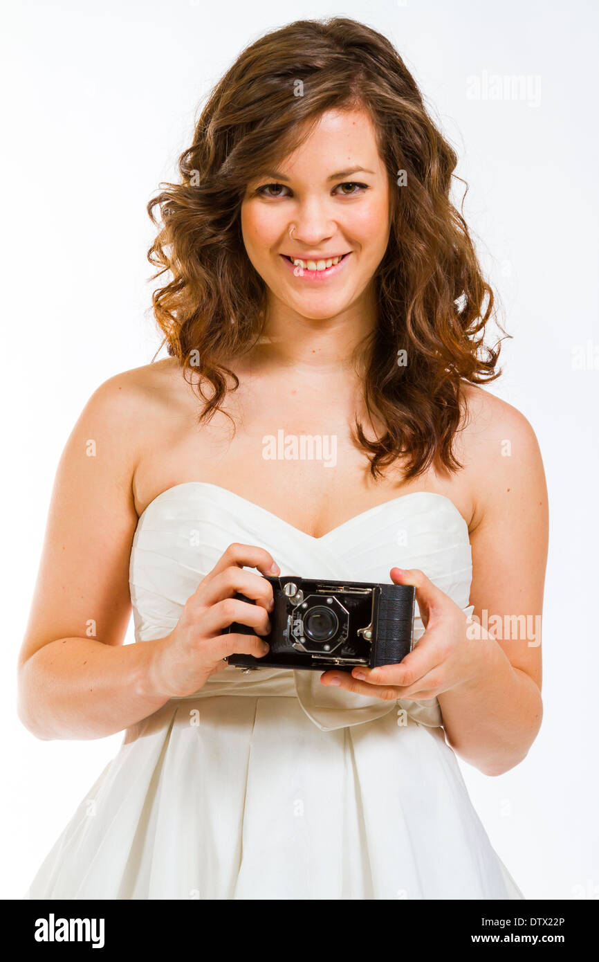 Une belle épouse tenant un appareil photo en studio contre un fond blanc. Banque D'Images