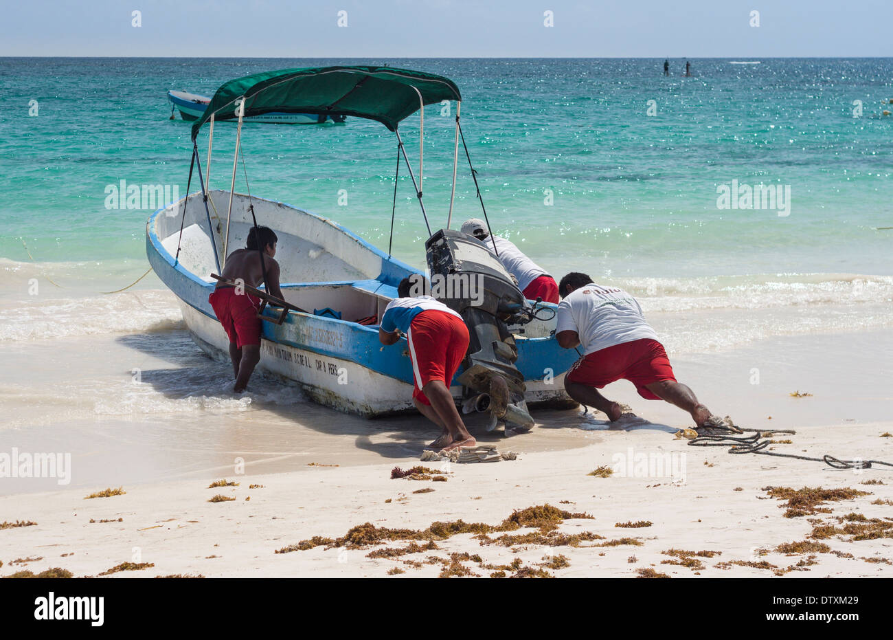 La grande poussée au large de la plage. Un équipage d'un bateau de pêche s'enfoncent dans le sable pour pousser leur bateau au large de la plage de Tulum. Banque D'Images