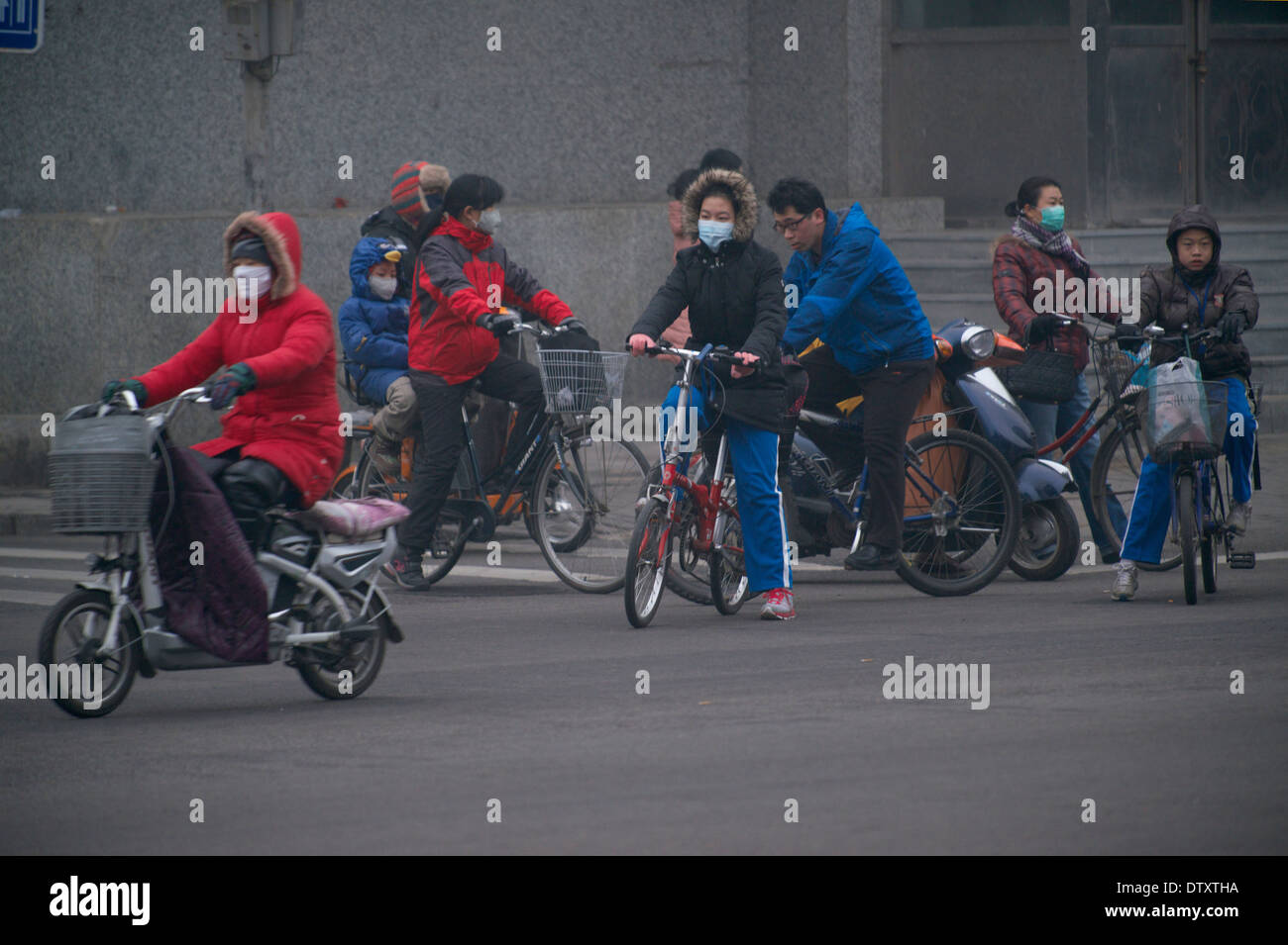 Les personnes portant des masques de la bicyclette le long d'une rue, sur un ciel voilé le matin à Beijing, Chine. 25-Feb-2014 Banque D'Images