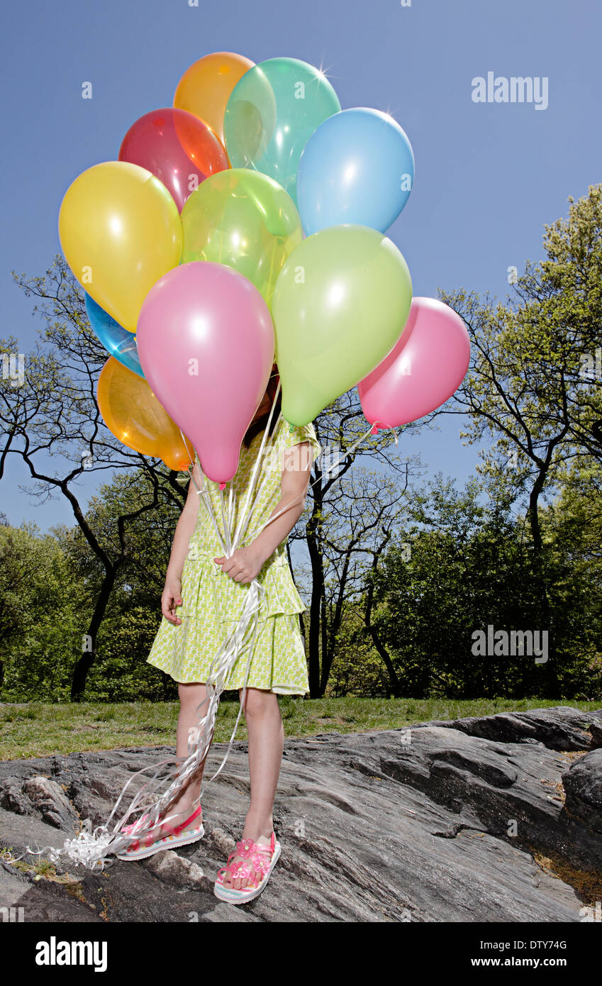 Mixed Race girl réalisation colorful balloons in park Banque D'Images