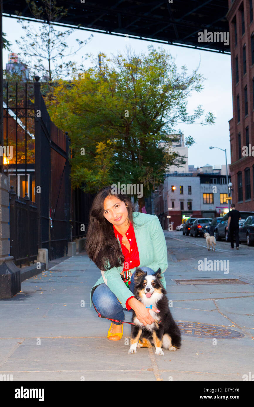 Mixed Race woman petting dog on city sidewalk Banque D'Images