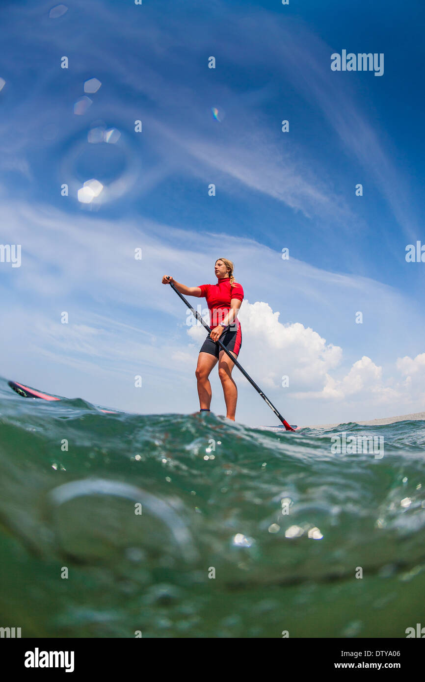 Une fille dans un rash vest paddleboards rouge dans les eaux claires du North Devon UK SUP (stand up paddleboarding) Banque D'Images