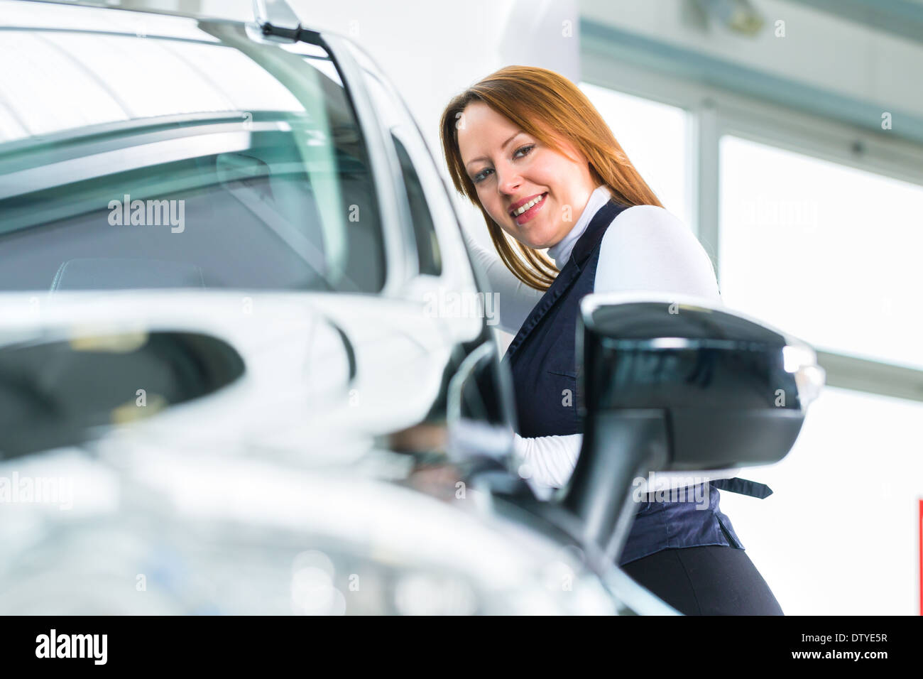 Jeune femme à côté d'une nouvelle voiture dans l'agence de voiture, de toute évidence, elle est l'achat d'auto, ou de faire un essai routier Banque D'Images