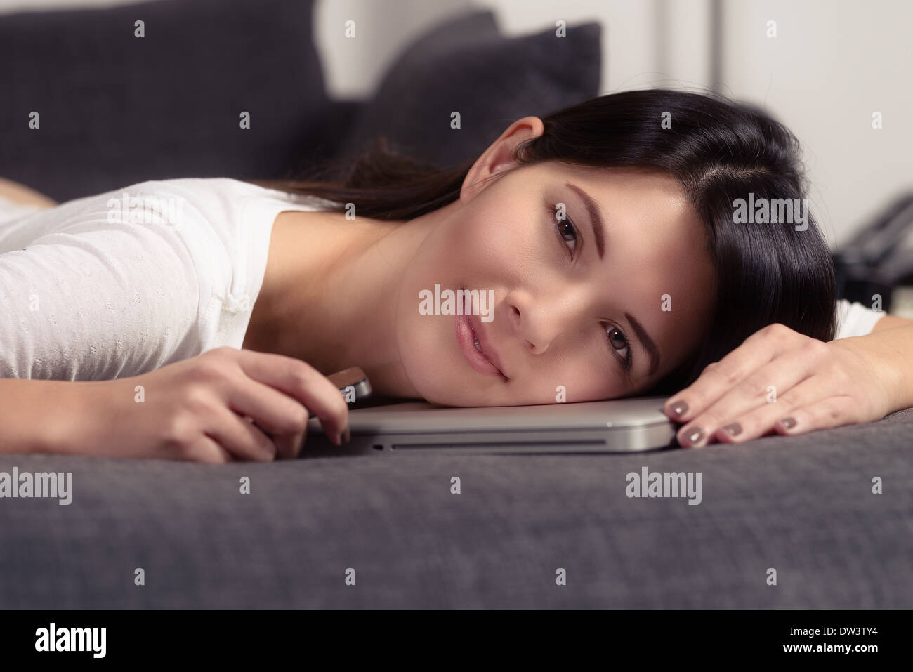 Charmante jeune femme avec sa tête placée sur un ordinateur portable smiling at the camera Banque D'Images