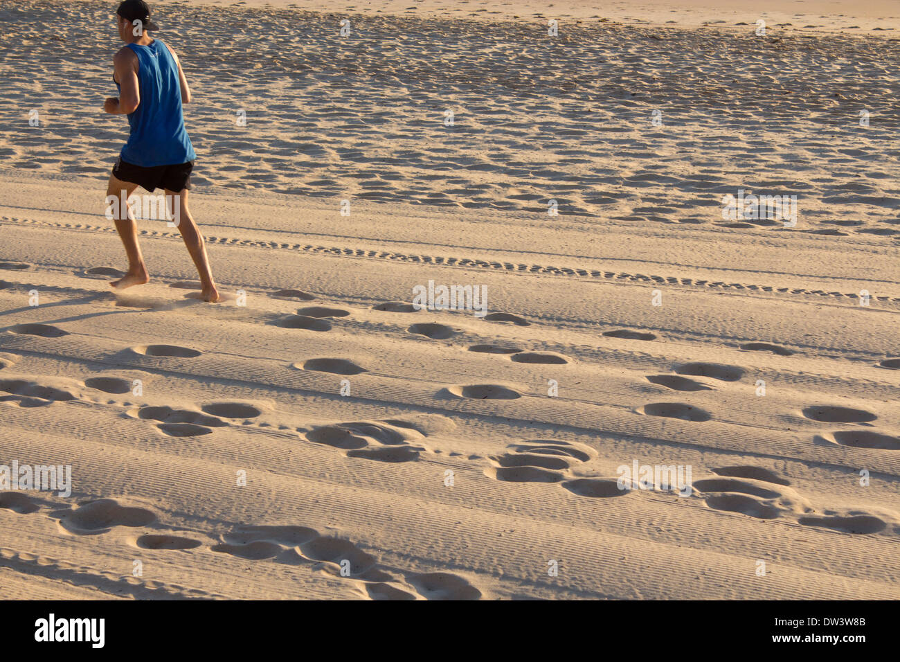 Empreintes et traces de pneu dans le sable à l'aube avec coureur en haut à gauche du châssis au Nord Steyne Manly Beach Sydney NSW Australie Banque D'Images